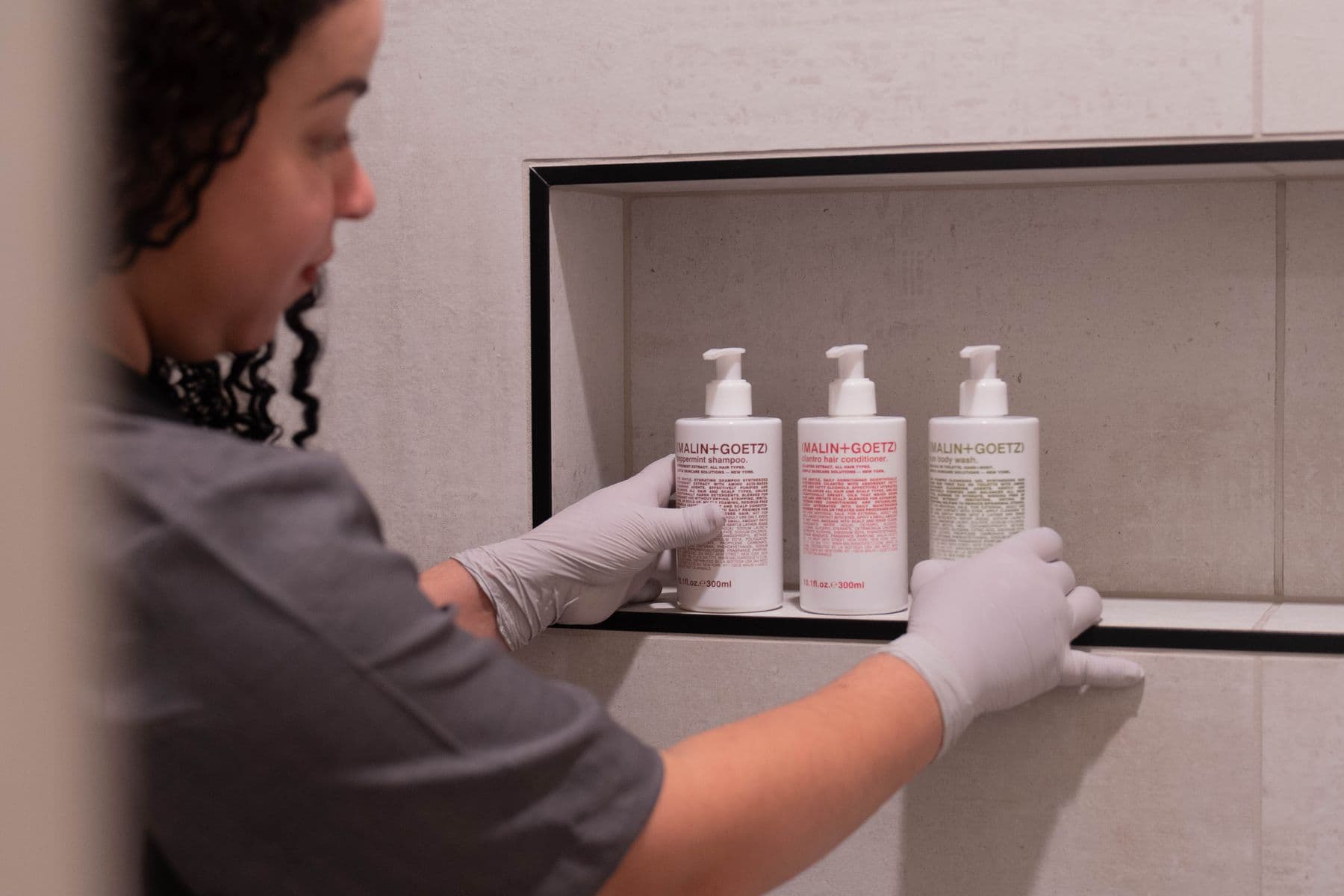 Nova cleaner restocking shampoo and soap bottles in a shower niche
