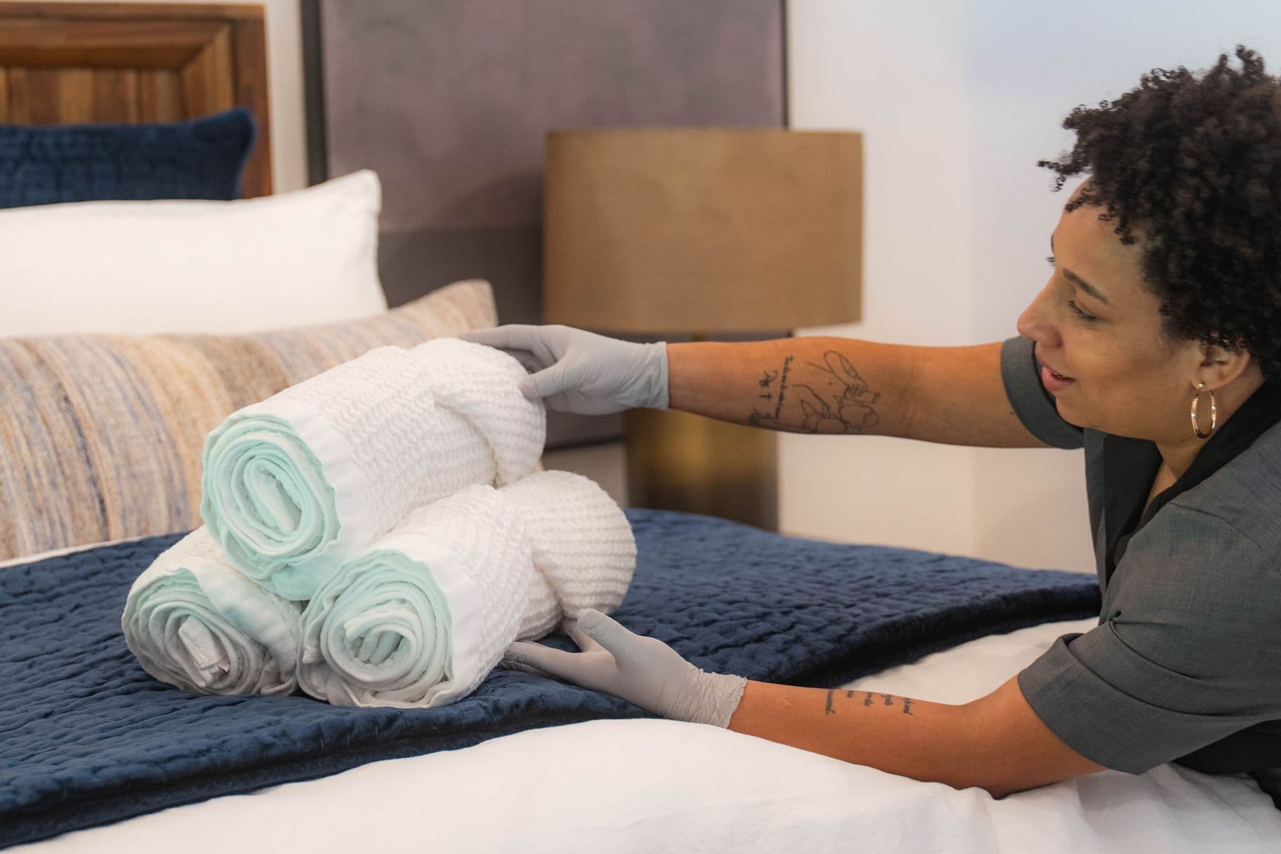 Nova cleaner placing rolled fresh towels on a made bed for the next guest