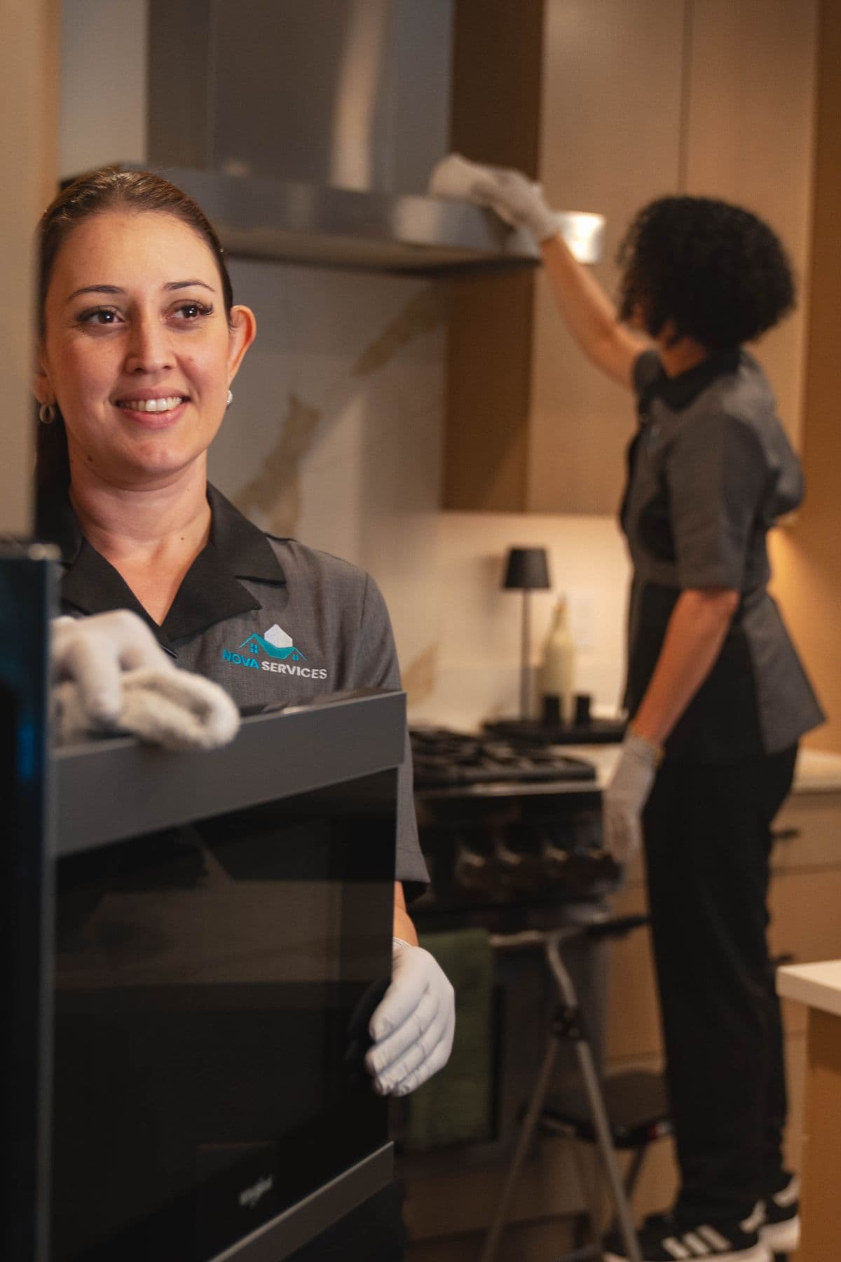 Two Nova Cleaning team members in grey uniforms cleaning a modern kitchen