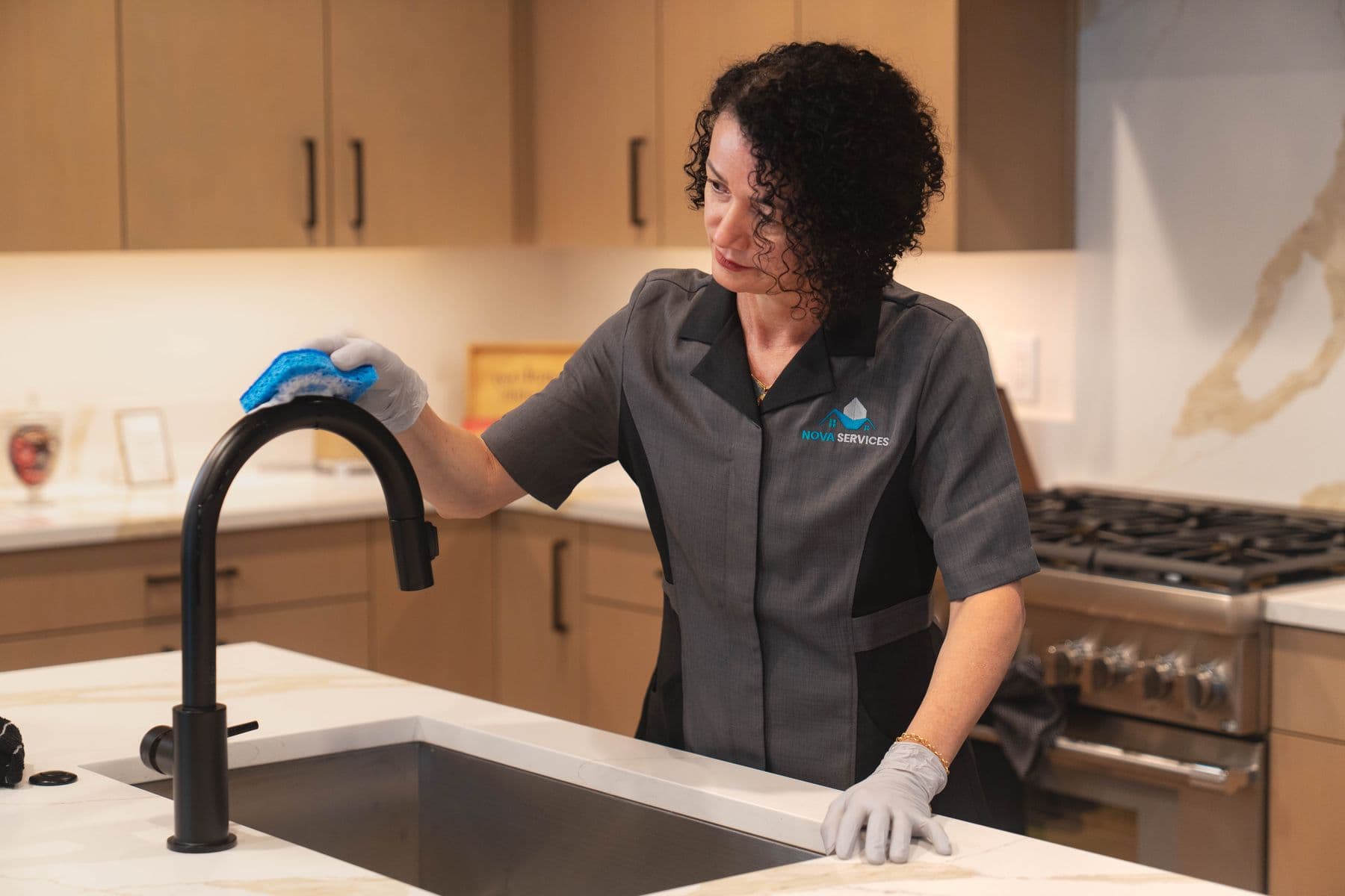 Nova cleaner in a grey uniform wiping down a kitchen counter beside the sink